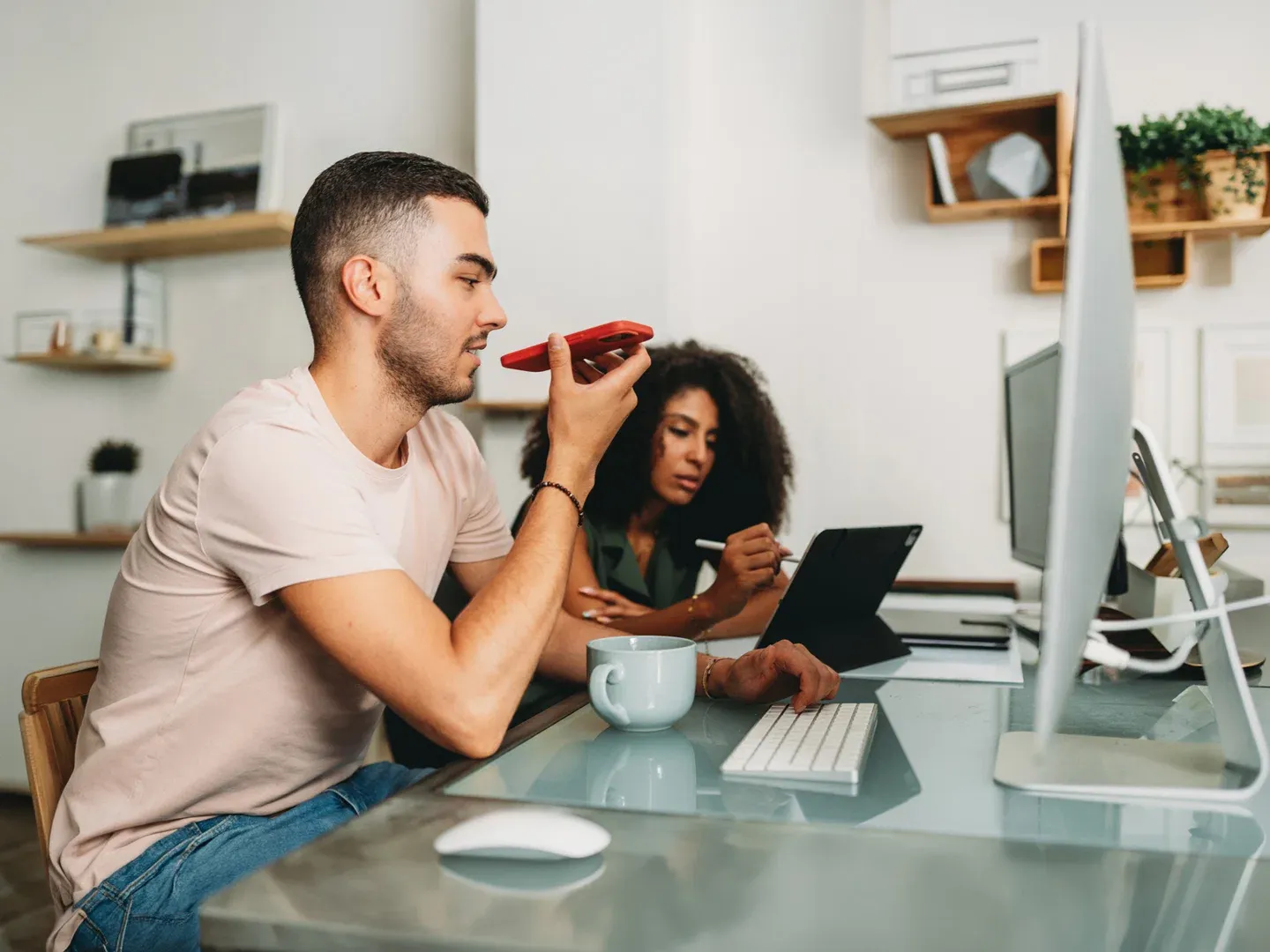 A man talking on his phone at a desk while a colleague works beside him on a tablet.
